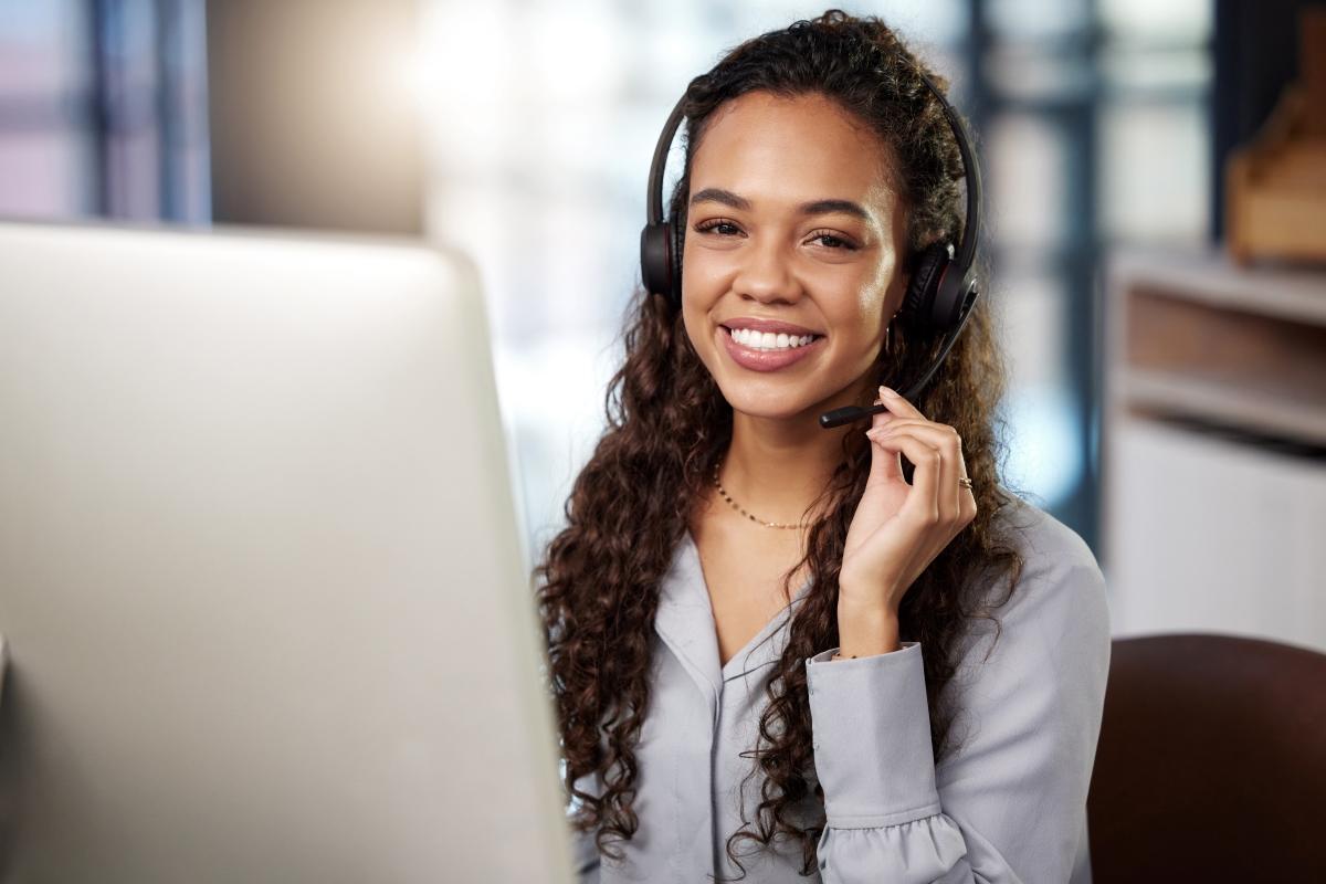 Young woman smiling while wearing headset while working on computer.