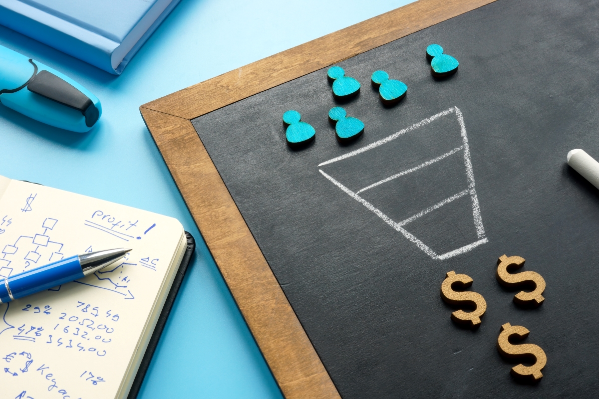 Wooden board with figures Wooden board on table with human alike figures an funnel drawn with chalk leading to dollar signs.