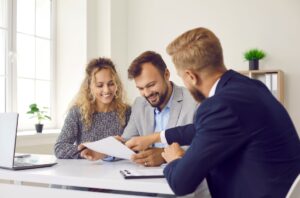Couple smiling as thry observe paperwork, man in suit points at paper and smiles, in office space.