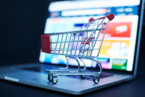 Small shopping cart placed on a laptop keyboard with a colorful screen in the background.