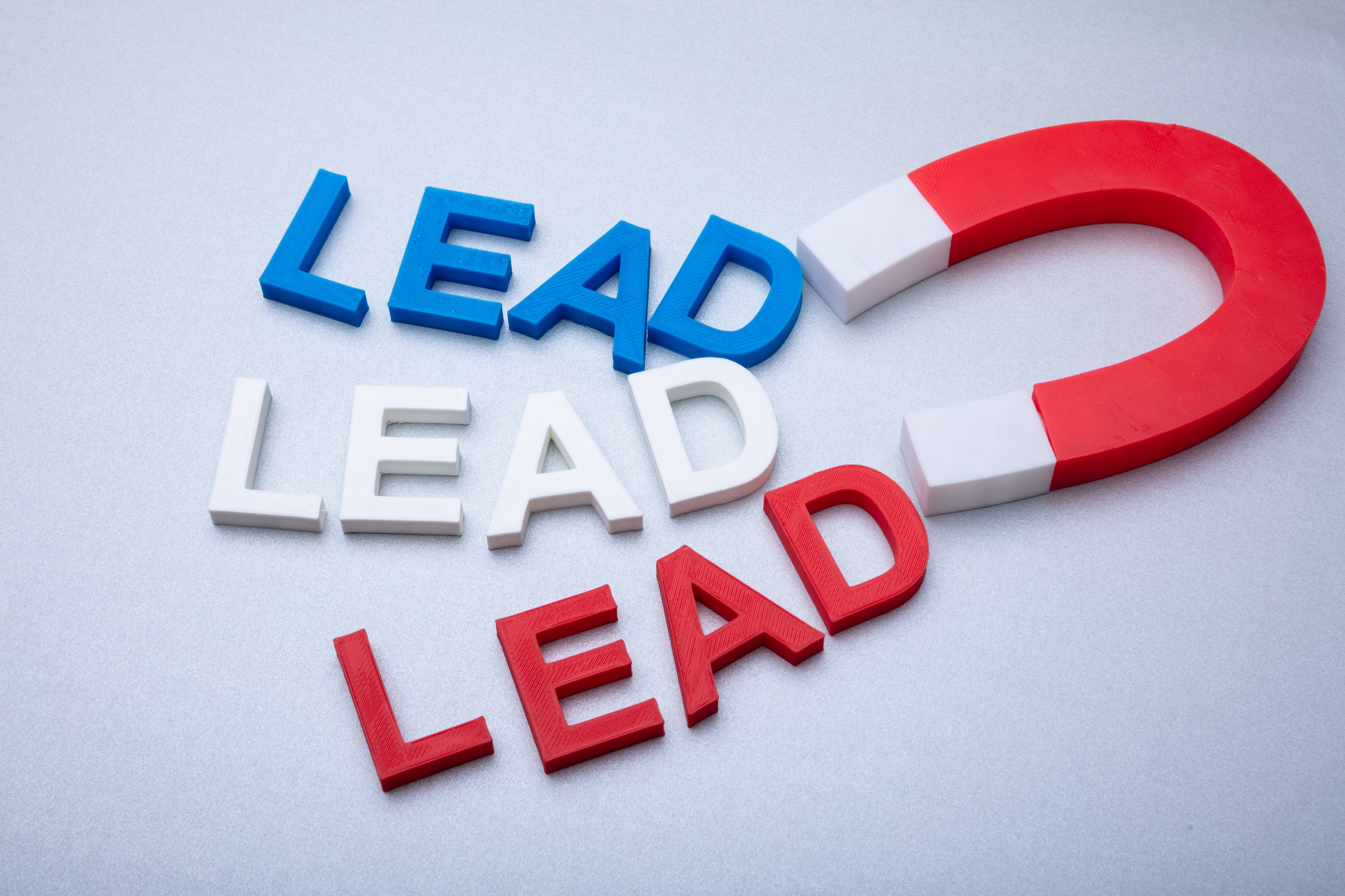 Red and Blue Magnet Attracting “LEAD” A red and white horseshoe magnet attracting the word "LEAD" in red, blue, and white colors arranged on a light gray surface.
