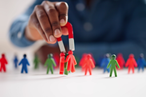 A hand holding a red and white magnet attracting red and green plastic figurines, with other figurines scattered on a white surface.