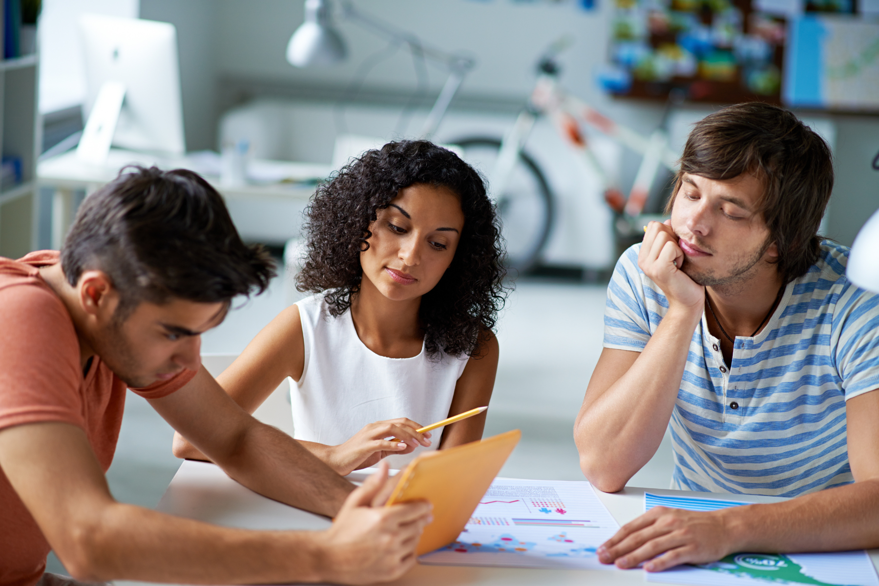 A group of young professionals collaborating in a modern office setting, reviewing documents and charts together.