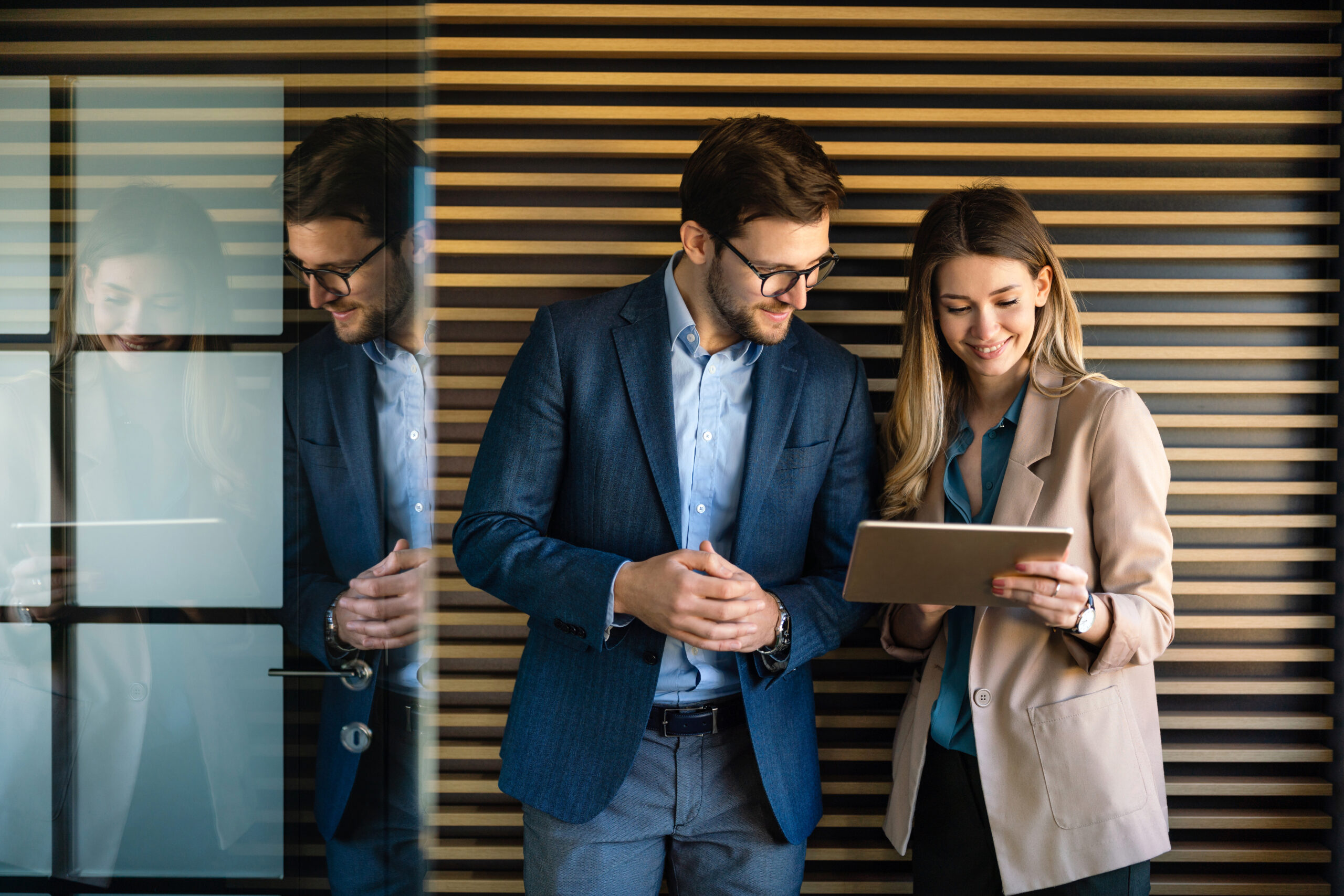 A business professional and a young woman looking at a tablet, discussing work in a modern office setting, symbolizing teamwork and mentorship.