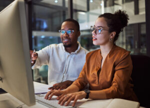 A man and a woman working together on a desktop computer, symbolizing collaboration and teamwork in a professional setting.