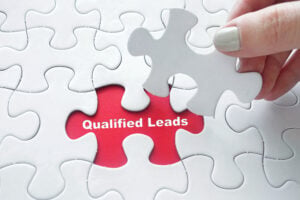 Close up of hand placing the last jigsaw puzzle piece with word Qualified Leads.