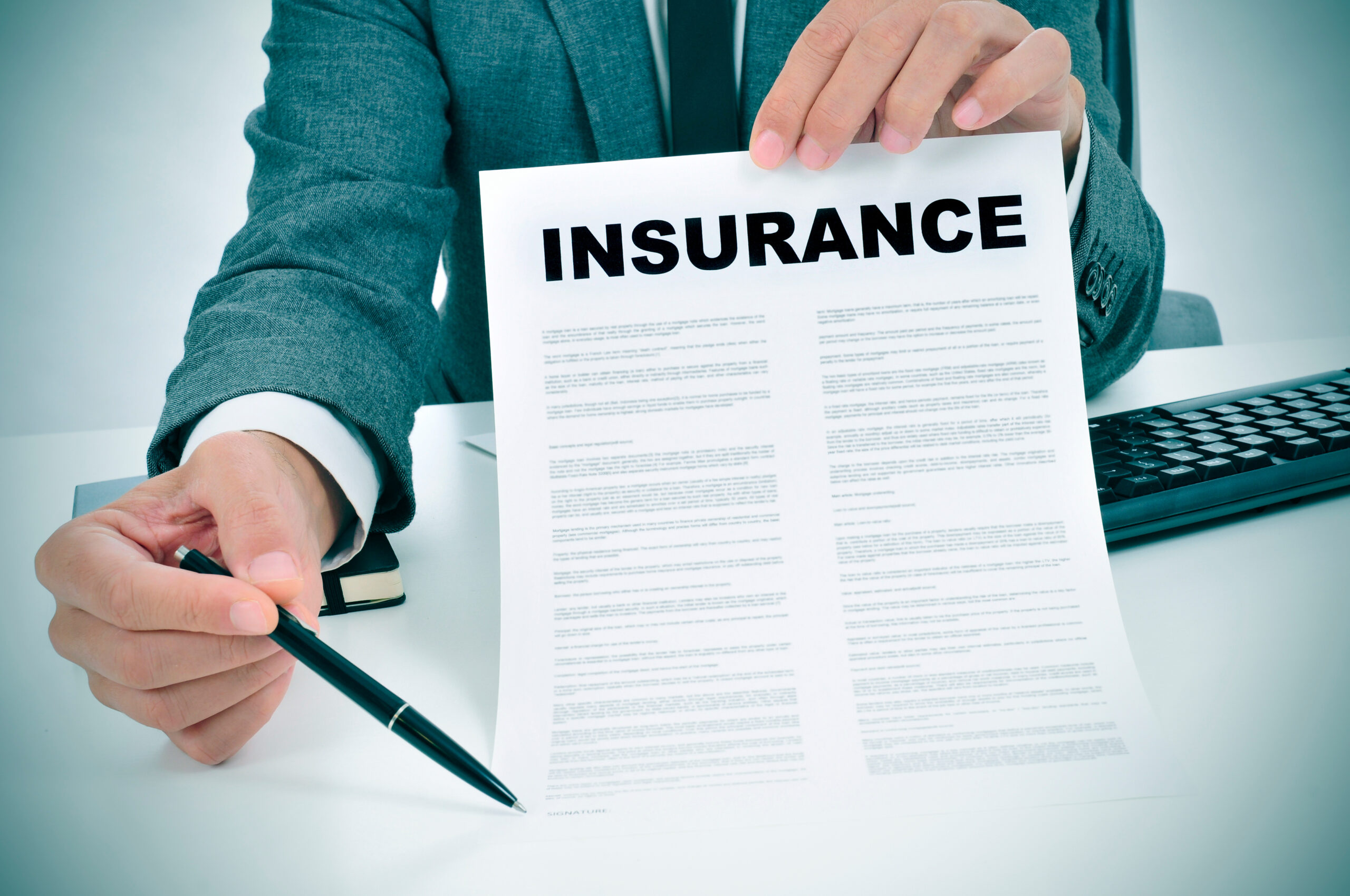 Man in suit in his office showing an insurance policy and pointing with a pen where the policyholder must to sign
