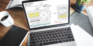 Laptop displaying a web design sketch with layout wireframes and notes for responsive mobile design.