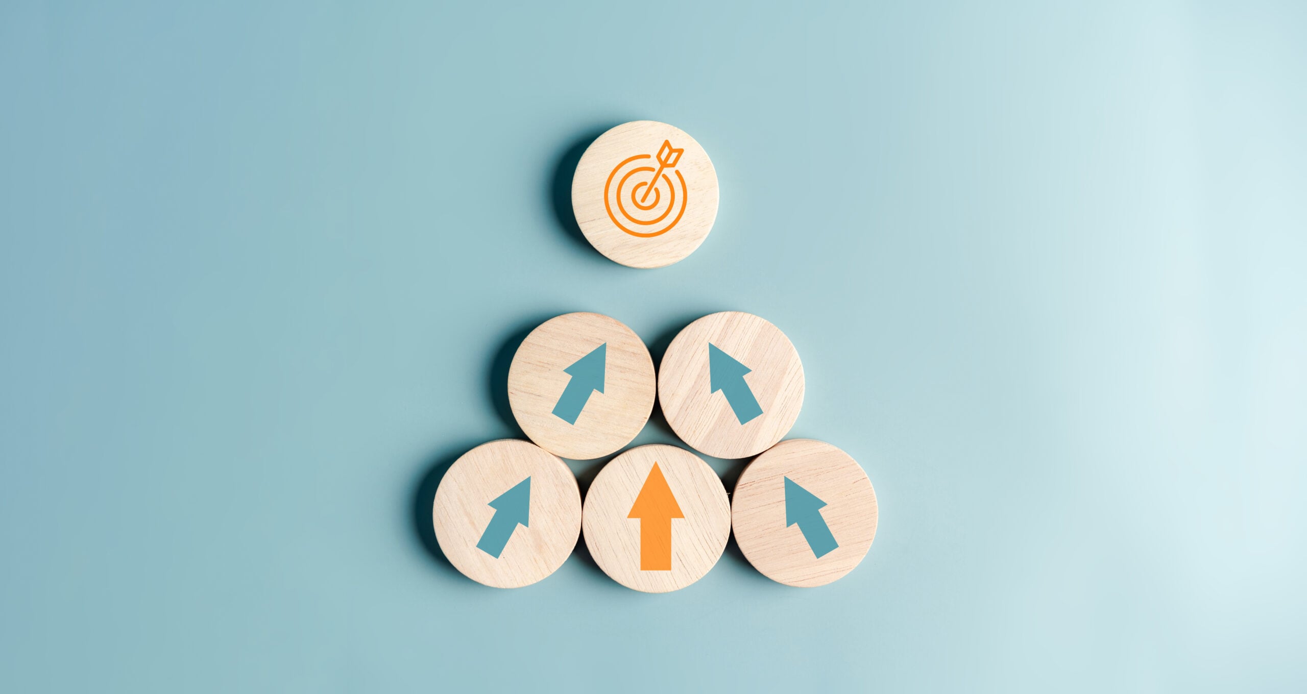 Wooden blocks arranged in a pyramid with arrows pointing upward toward a target icon, symbolizing business goals and growth.