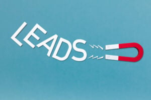 A minimalist graphic on a blue background showing the word “LEADS” being pulled toward a red-and-white horseshoe magnet. The image visually represents attracting or capturing customer leads.